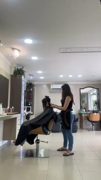 Cabeleireira cortando o cabelo de uma cliente de capa preta, no salão